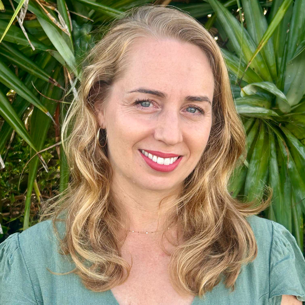 A head shot photo of Lisa Richards wearing a green shirt with pandanus in the background 